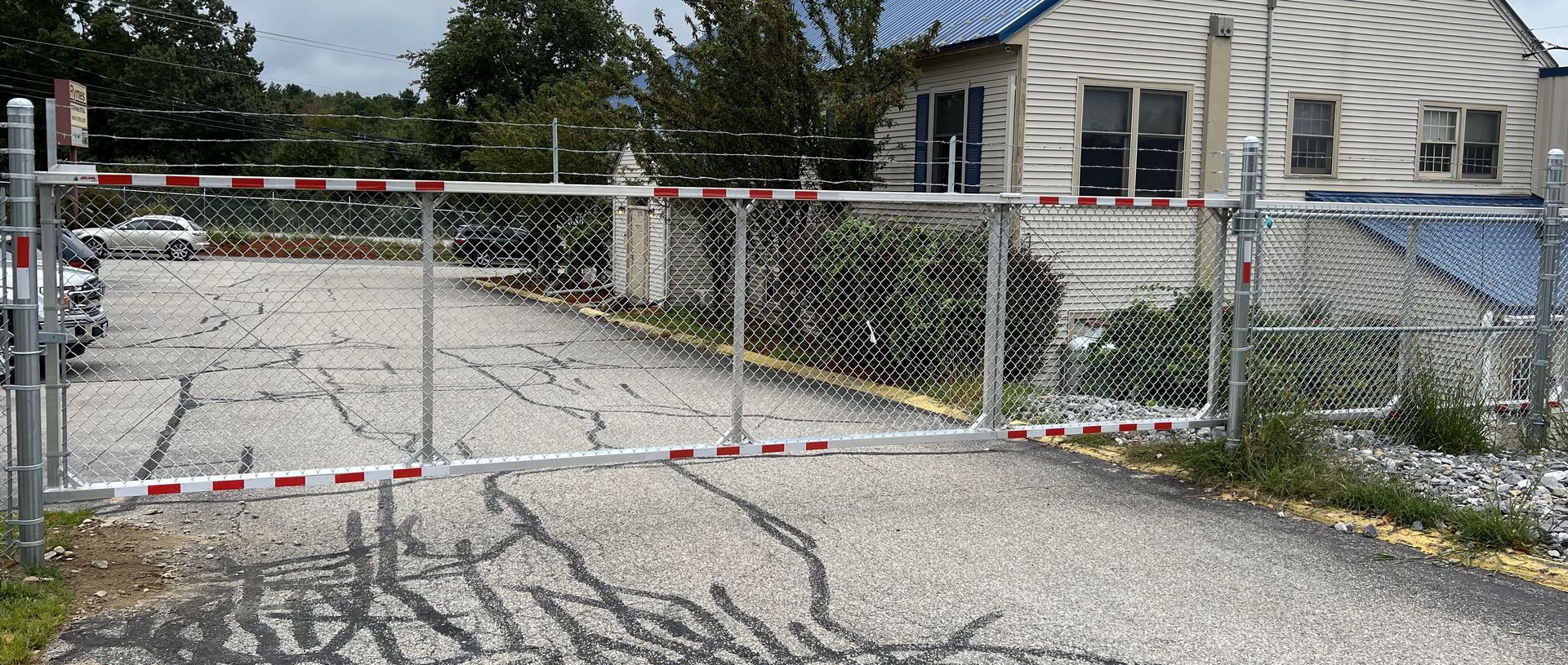 A gate is closed on a gravel road in front of a house.