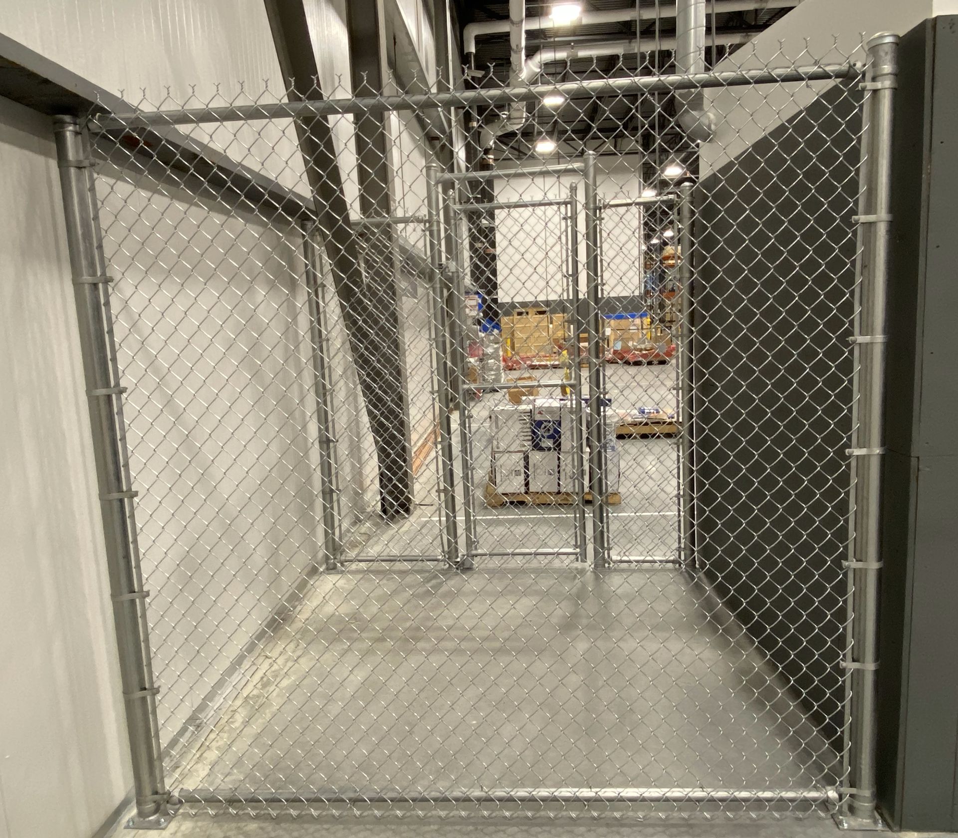 A chain link fence is surrounding a room in a warehouse.