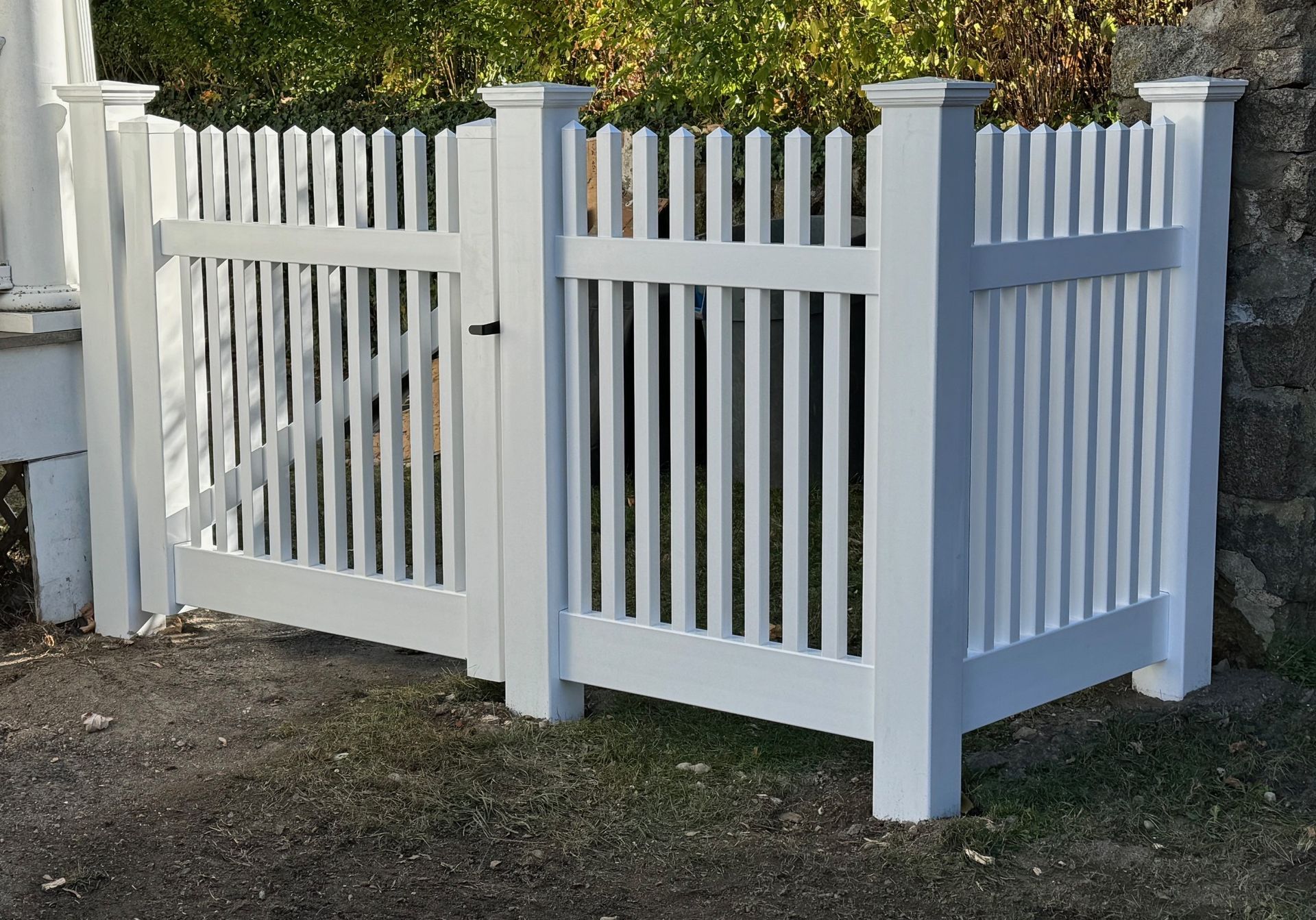 A white picket fence is sitting next to a stone wall.