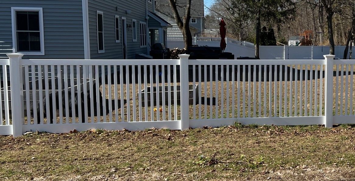 A white fence surrounds a grassy yard in front of a house.