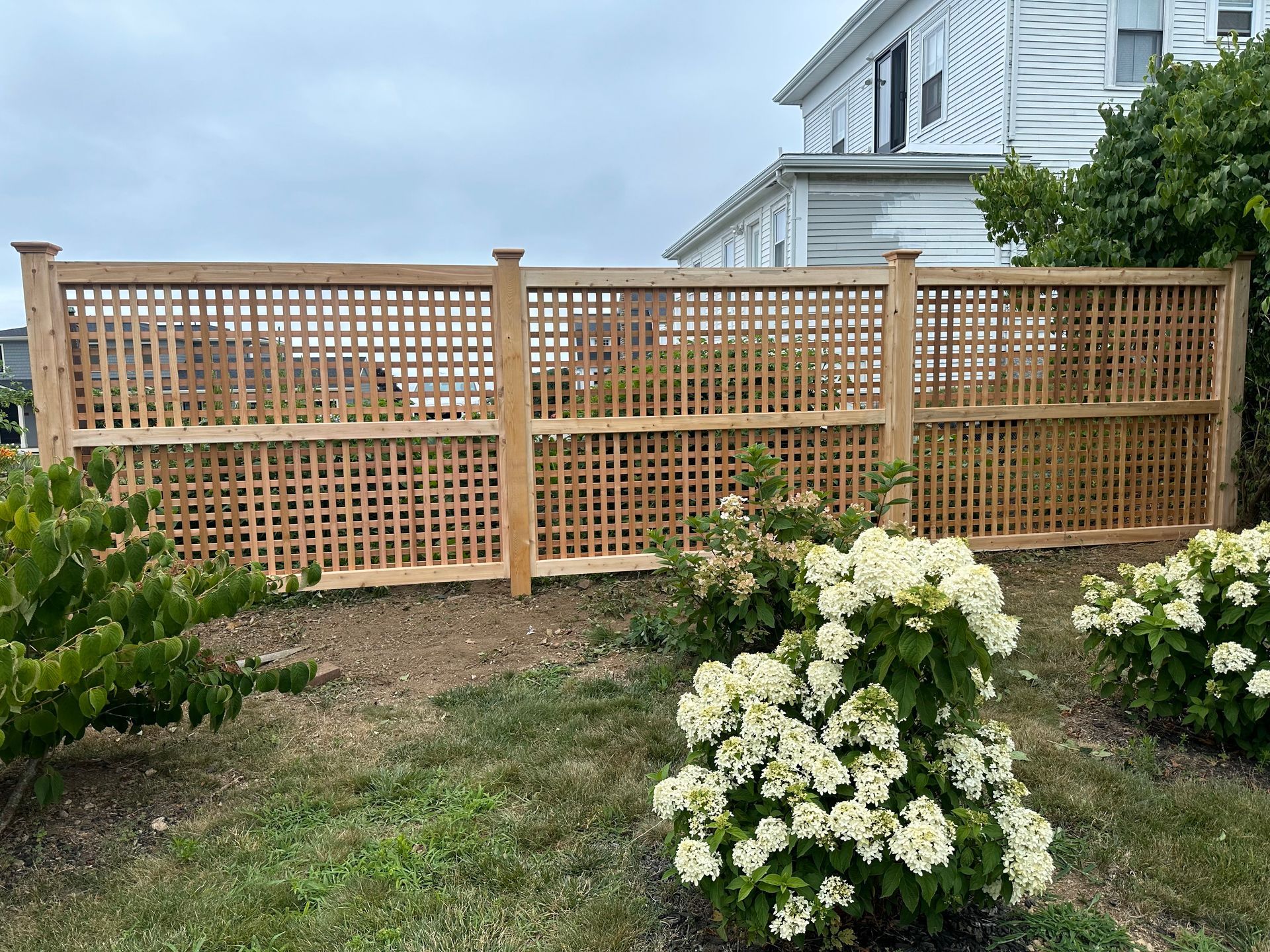 A wooden fence is surrounded by flowers and bushes in front of a house.