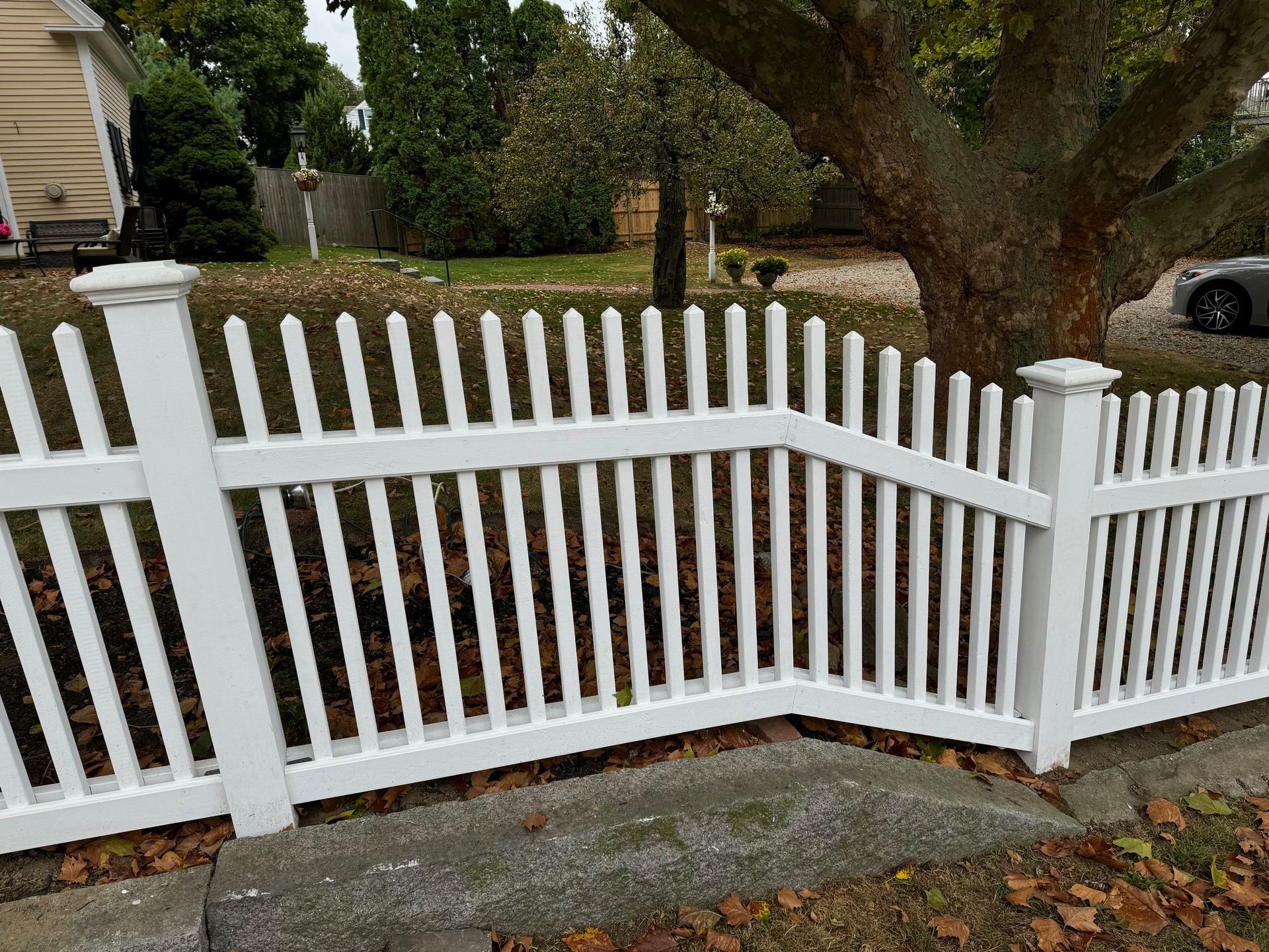 A white picket fence is sitting next to a tree in front of a house.