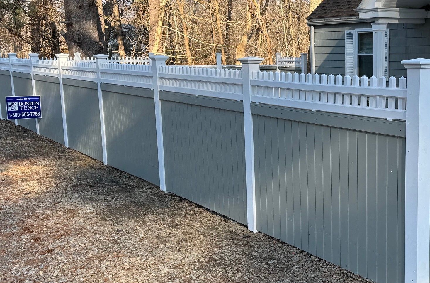 A white picket fence surrounds a driveway in front of a house.