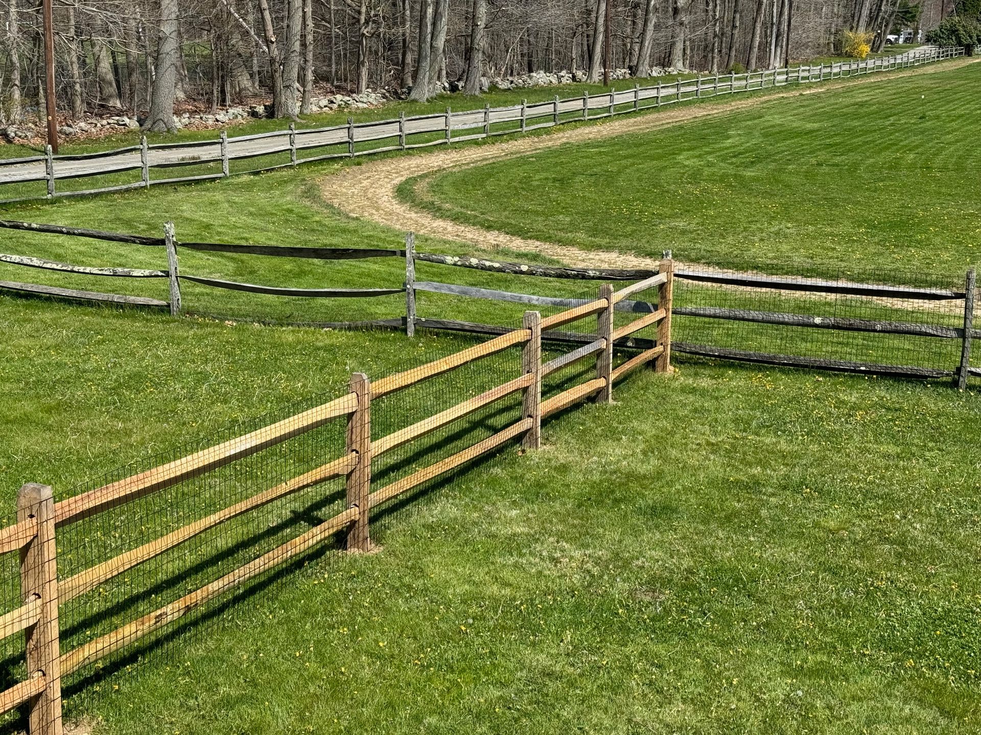 A wooden fence surrounds a grassy field with a dirt road going through it.