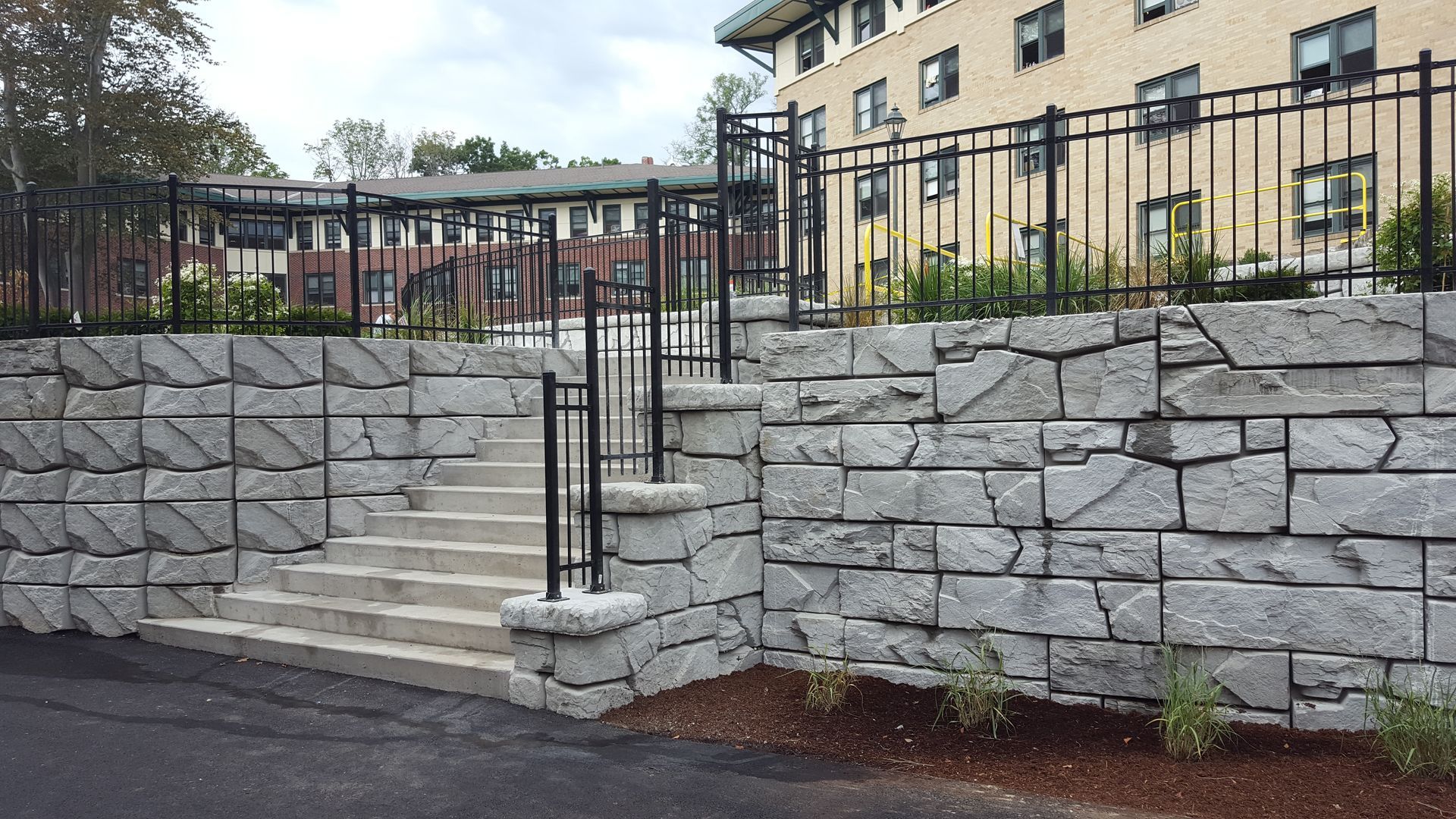 A stone wall with stairs and a fence in front of a building
