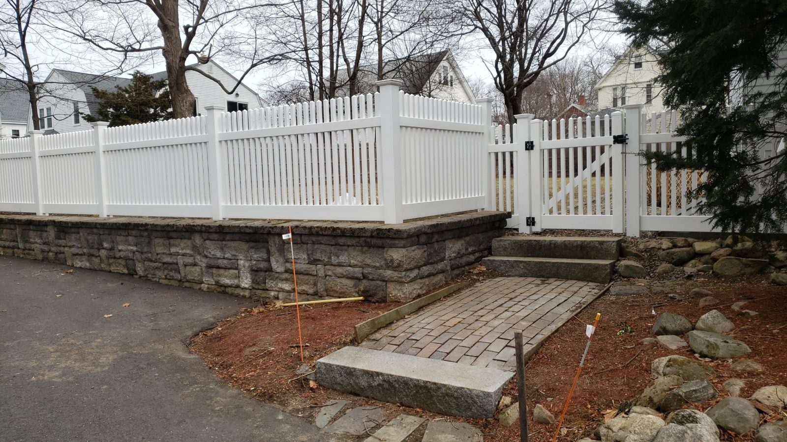 A white picket fence surrounds a stone wall and a stone walkway.