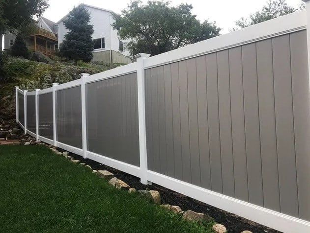 A gray and white fence surrounds a lush green yard.