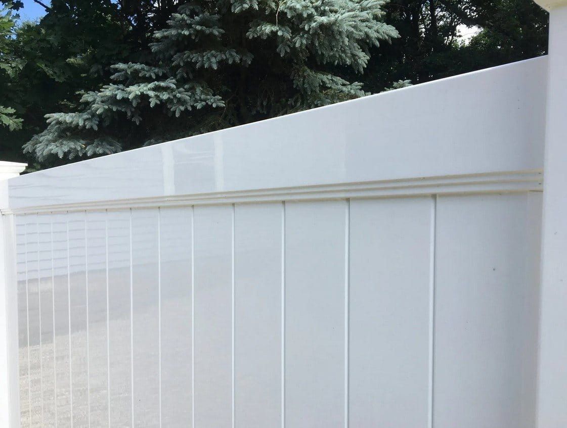 A close up of a white fence with trees in the background.