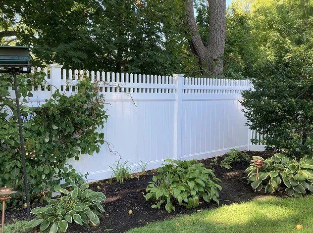 A white fence is surrounded by trees and bushes in a backyard.