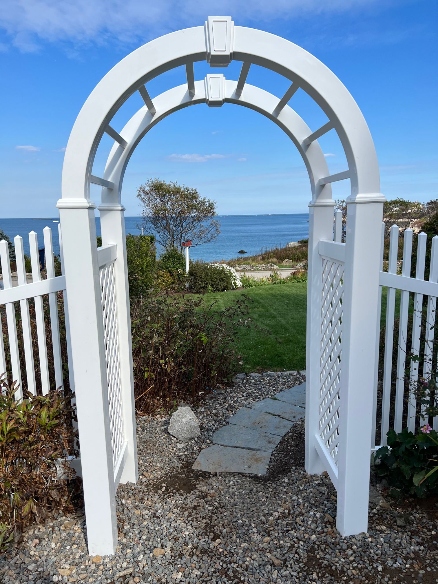 A white archway with a white picket fence leading to the ocean