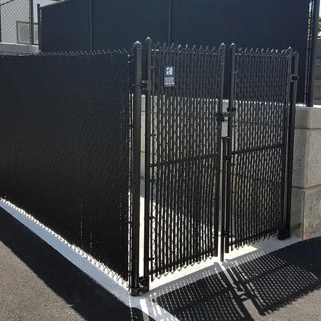 A black chain link fence with a gate leading to a parking lot