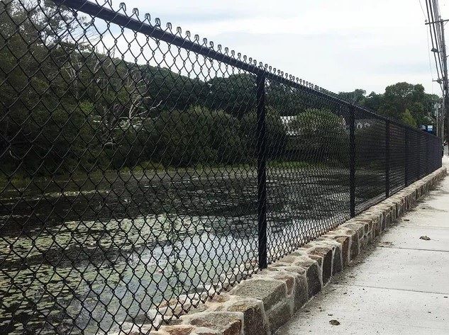 A chain link fence along a sidewalk next to a body of water.