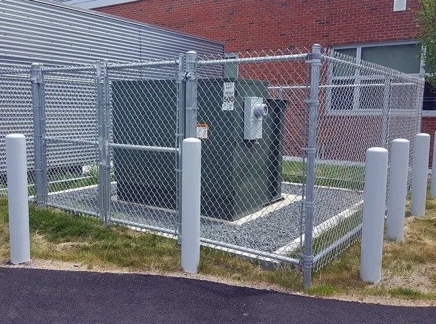 A transformer is behind a chain link fence.