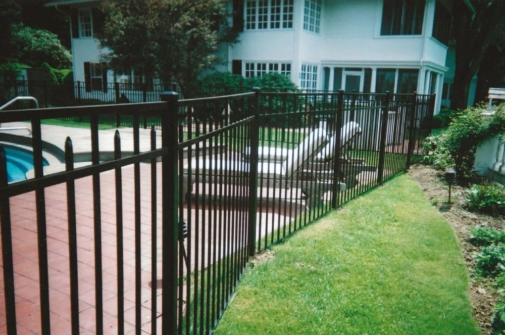 A black fence surrounds a swimming pool in front of a house