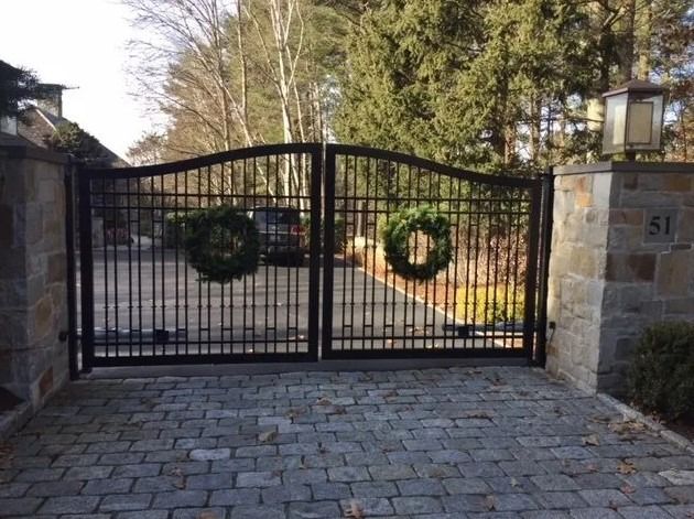 A black gate with two wreaths on it is open to a driveway.