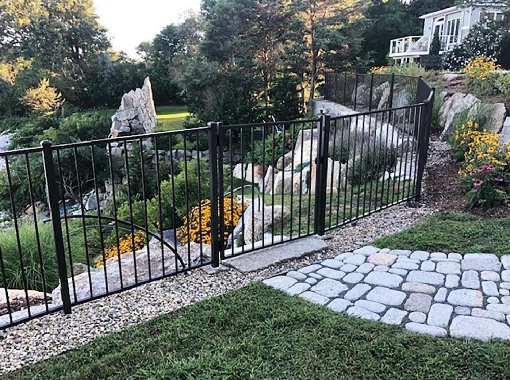 A wrought iron fence surrounds a stone walkway in a garden.