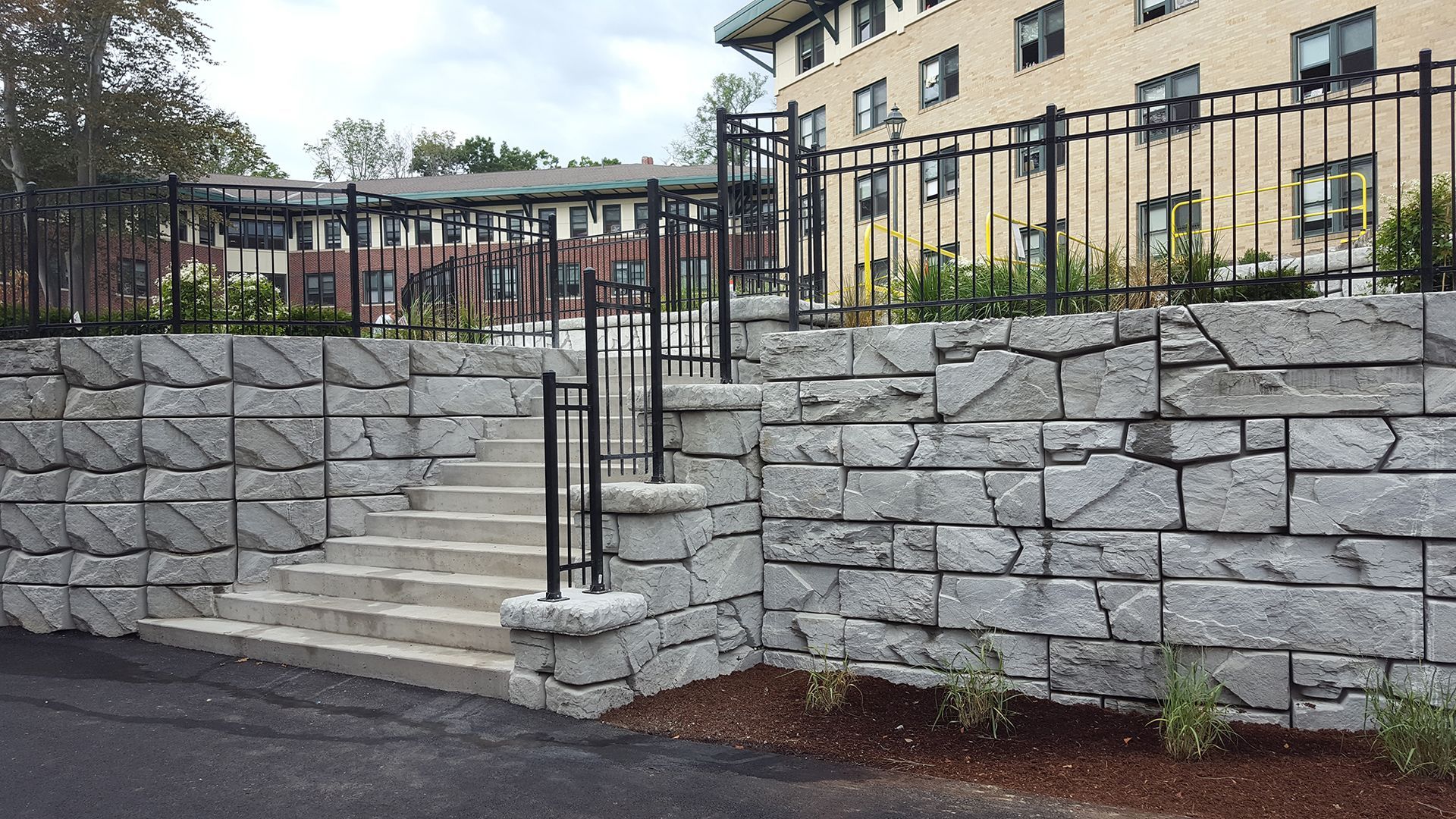 A stone wall with stairs and a fence in front of a building