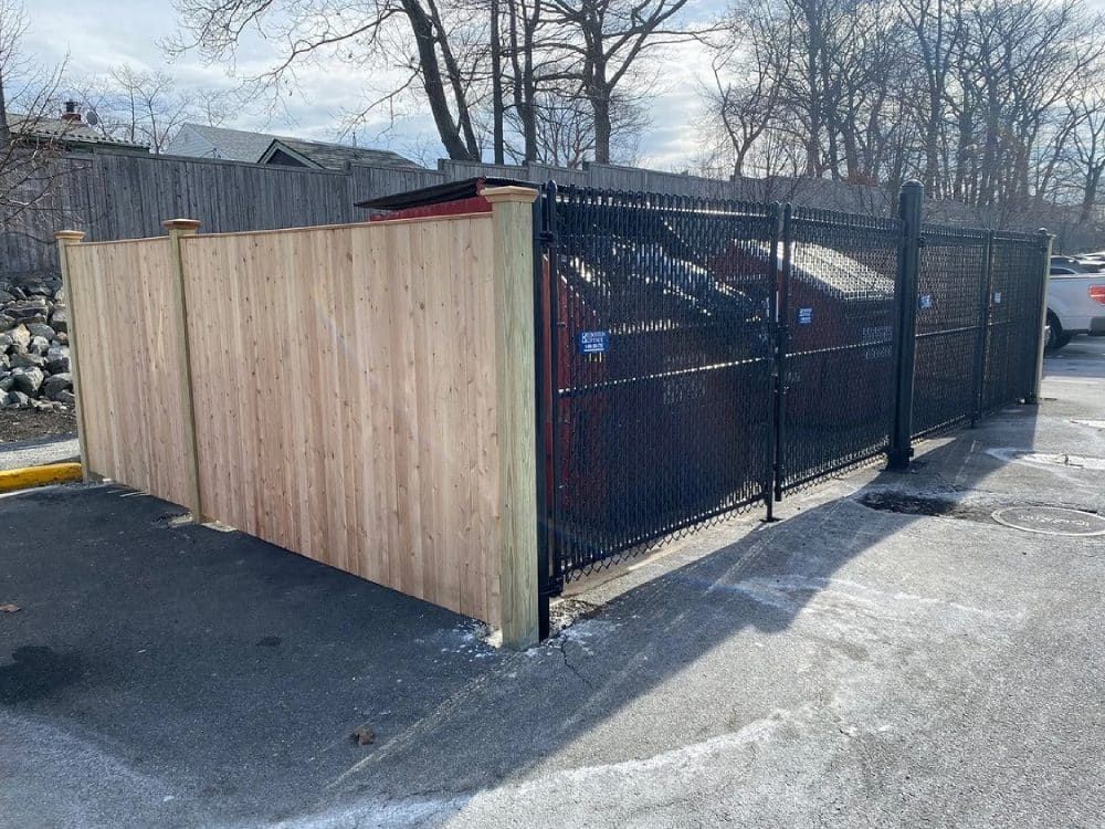 A wooden fence is surrounding a trash can in a parking lot.
