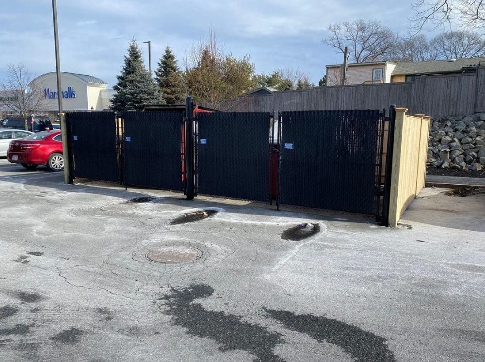 A red car is parked in front of a fence in a parking lot.