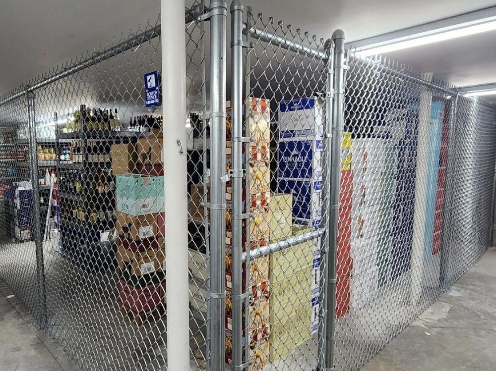 A chain link fence surrounds a room filled with shelves and boxes.