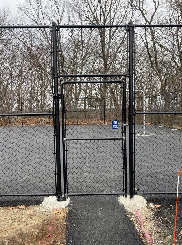 A chain link fence with a gate leading to a basketball court.