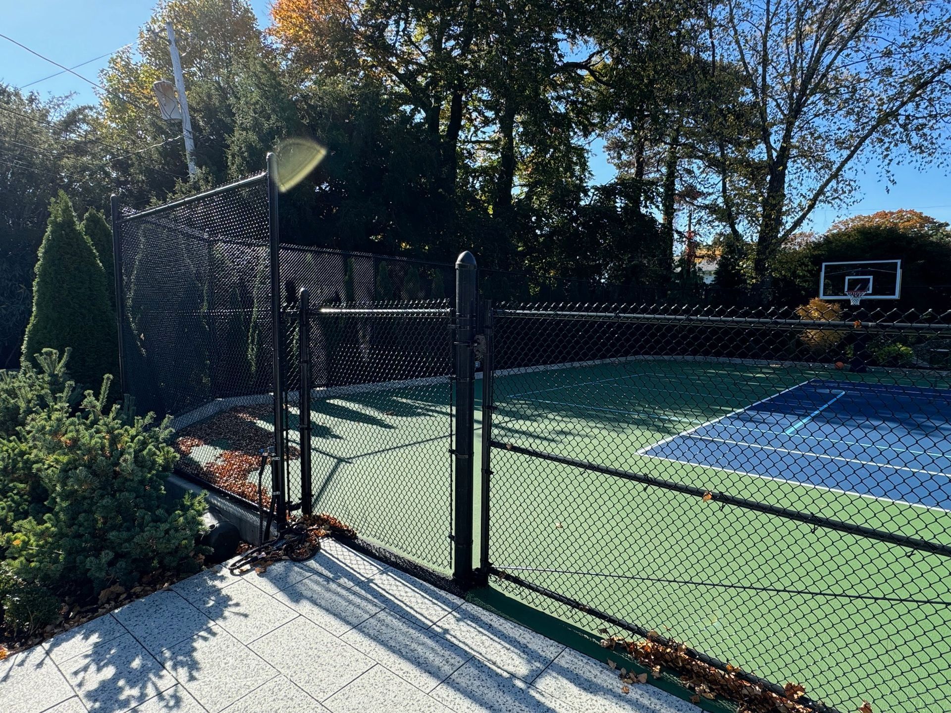 A tennis court with a basketball hoop behind a chain link fence.
