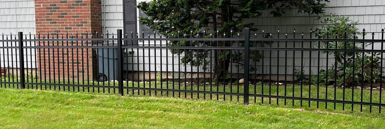 A black metal fence surrounds a lush green lawn in front of a brick house.