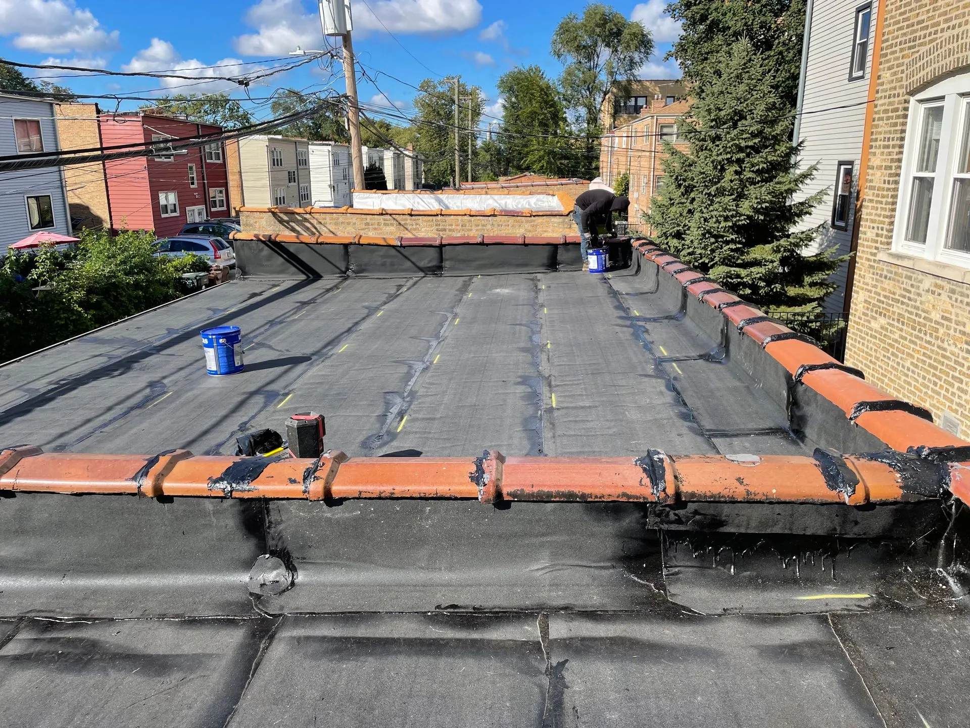 Flat roof with terracotta trim, a person working, buckets, and buildings in the background.