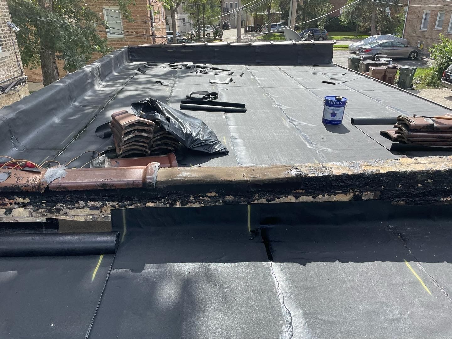 Flat roof partially covered with black roofing material, tools, and stacked tiles.