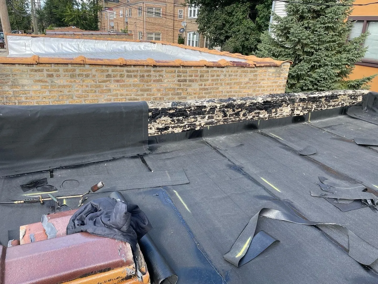 Damaged flat roof with peeling black roofing material and brick wall.