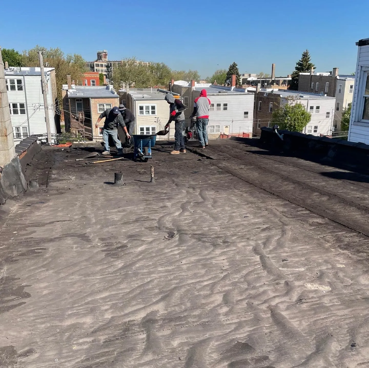 Construction workers repairing a flat roof on a sunny day in an urban neighborhood.