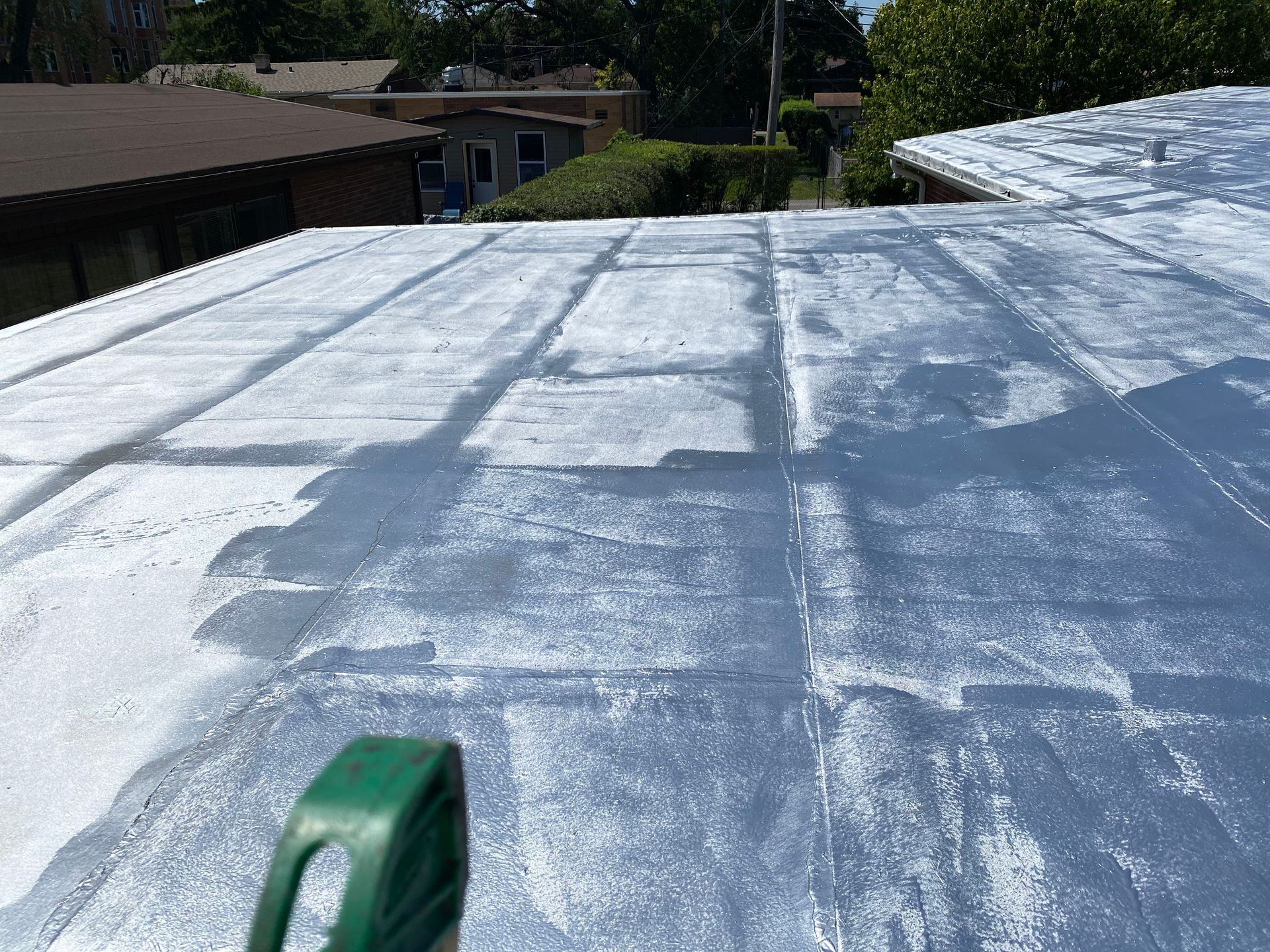 Overhead view of a flat, silvery roof; a green tape measure lies on the surface.