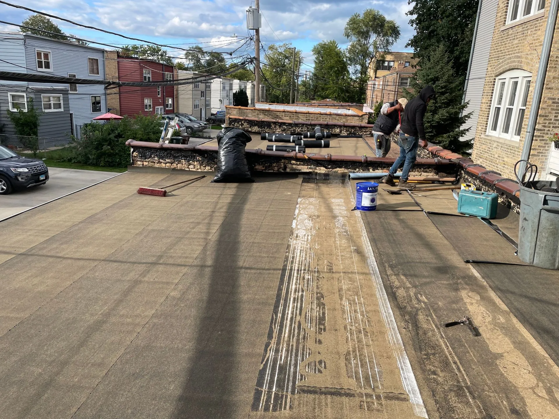 Roofers working on a flat roof. They are installing roofing materials with tools.