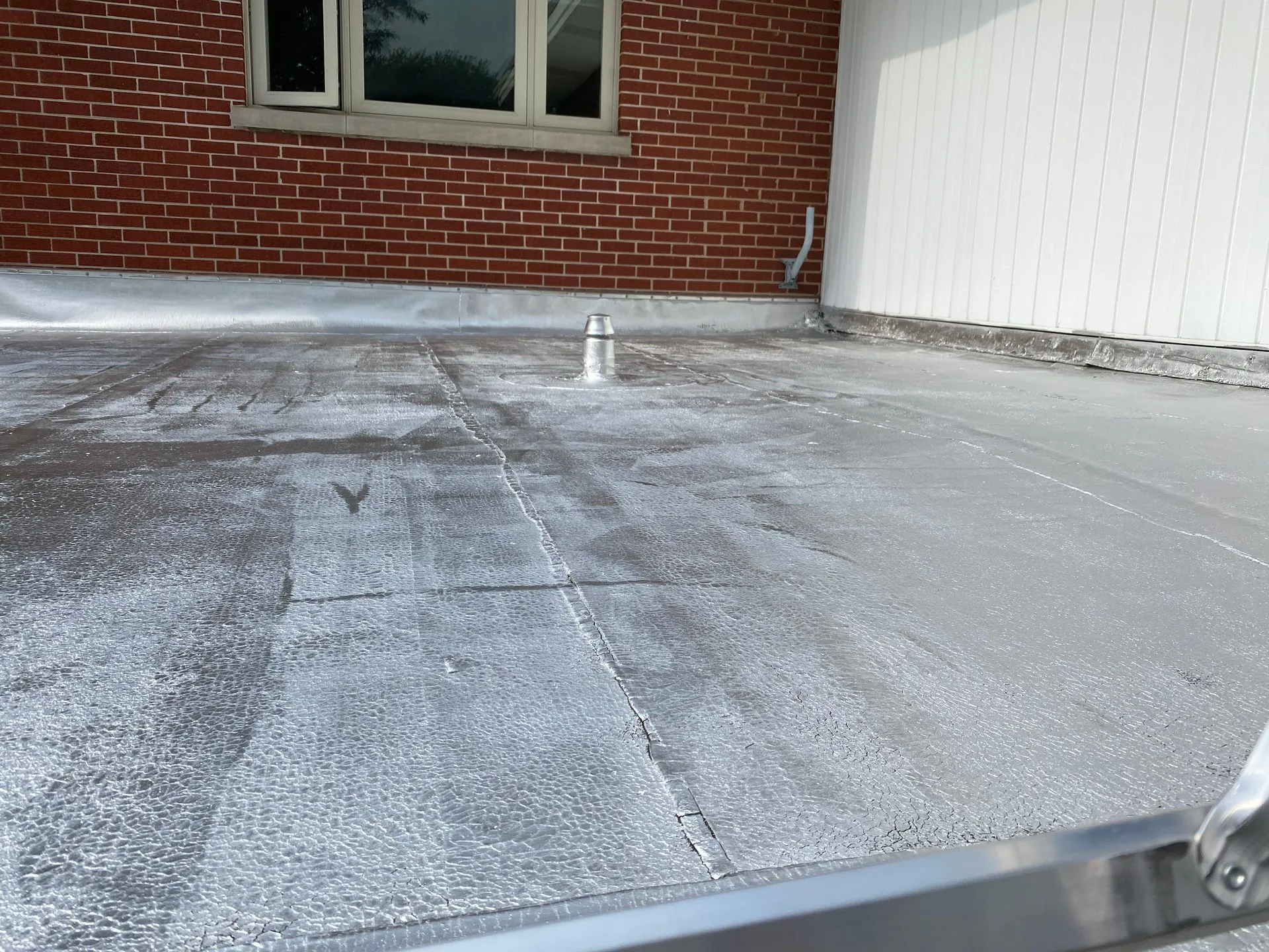 Flat roof with a coating. Brick building on the left, white wall on the right.