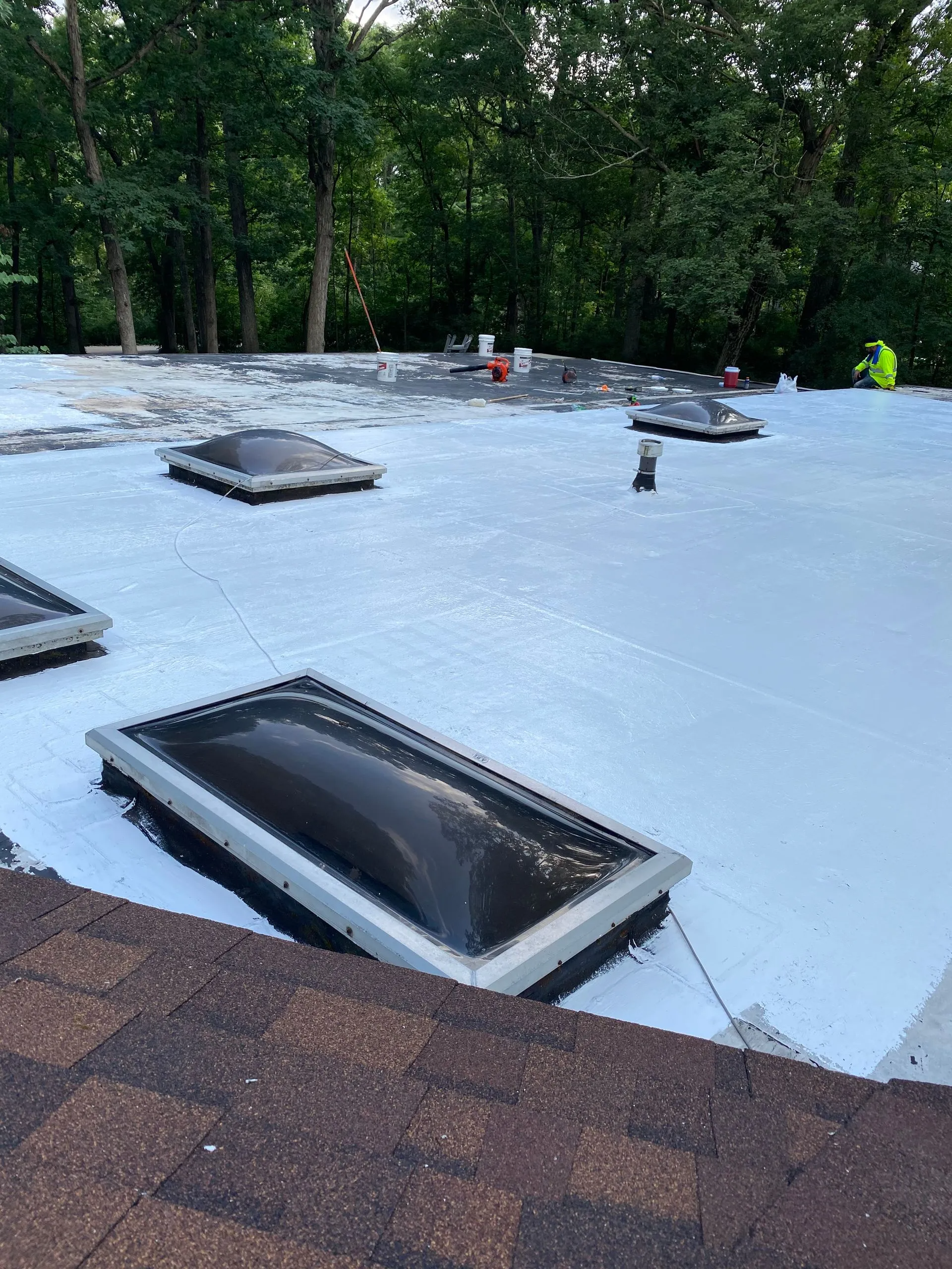 Flat roof with multiple skylights and a worker. The roof is white and has a brown shingle edge.