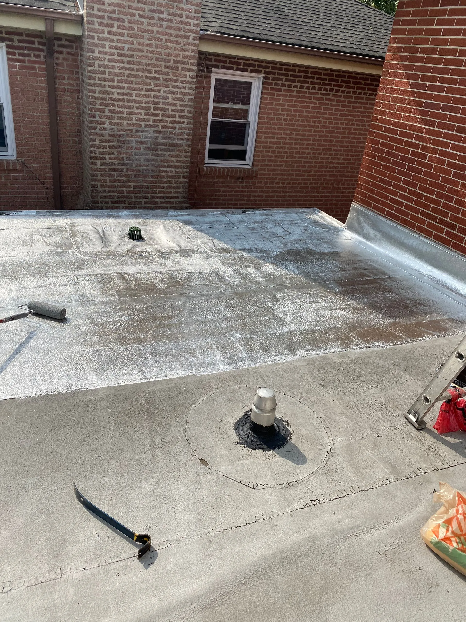 Flat roof with coating, vents, brick building in the background, gray and white.