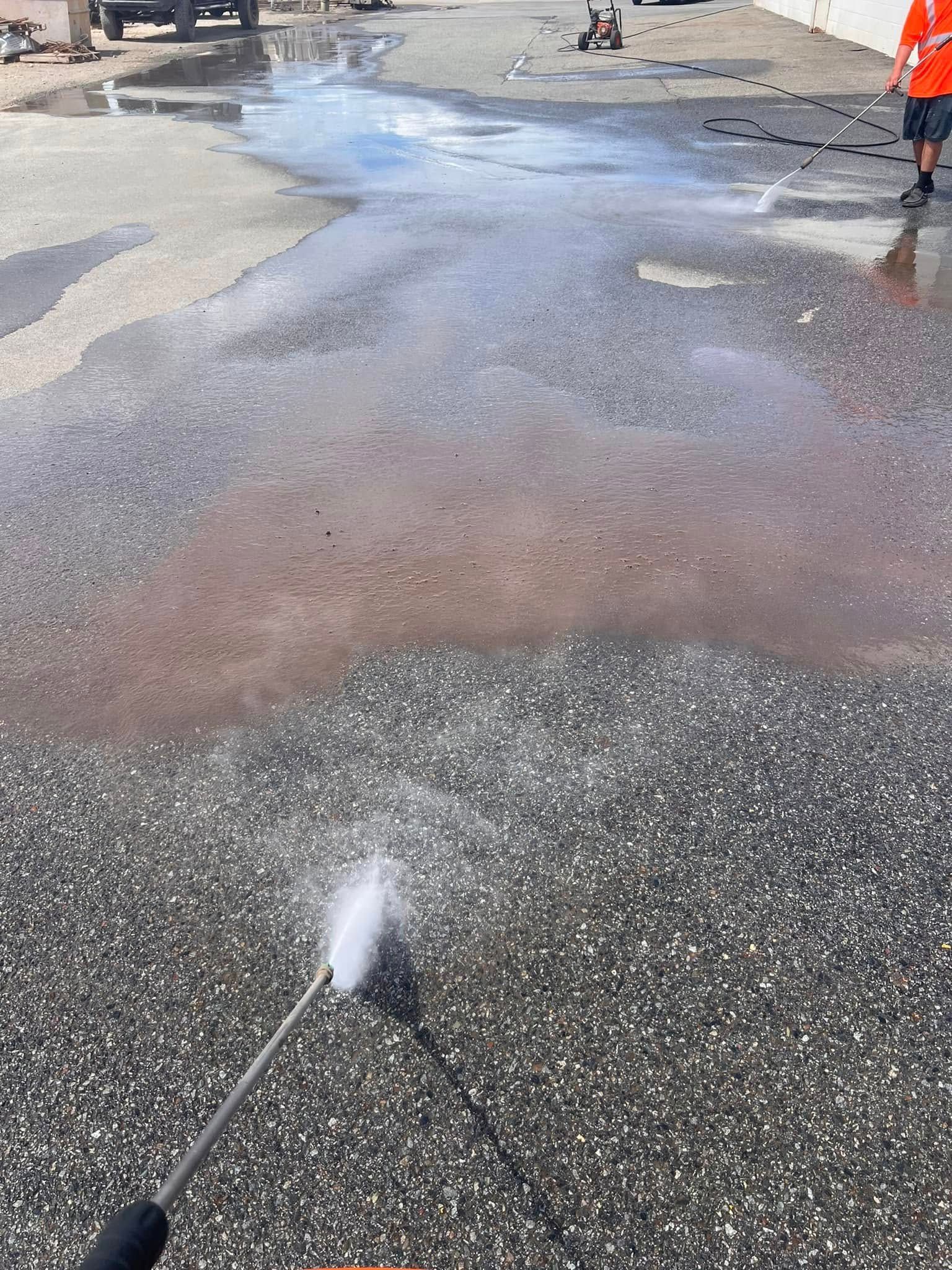 A person is using a high pressure washer to clean a puddle on the ground.