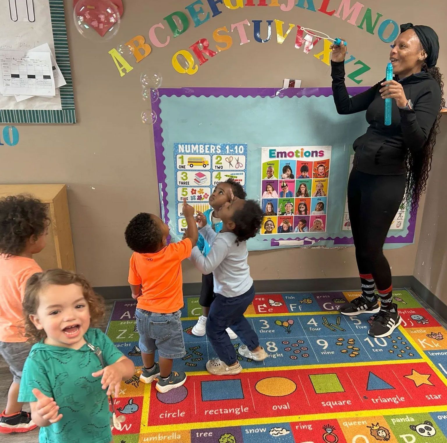 A group of children are playing in front of a bulletin board that says emotions