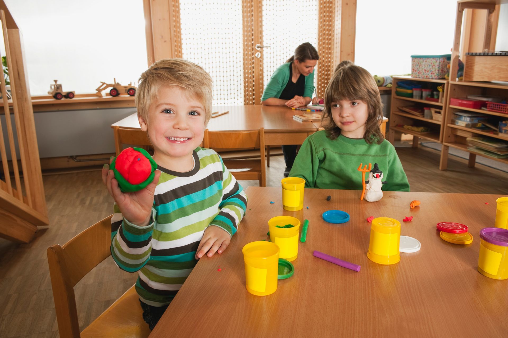 A boy and a girl are sitting at a table playing with play dough.