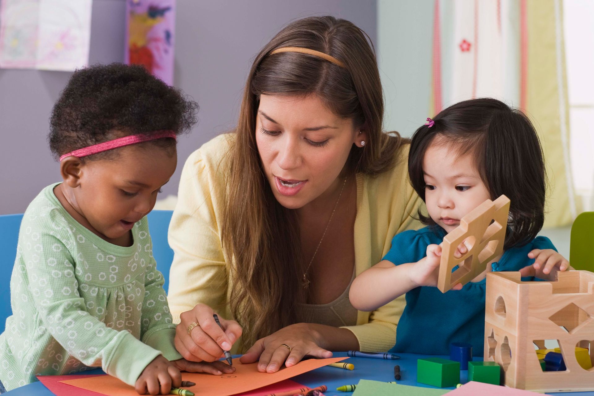 A woman is playing with two young girls at a table.