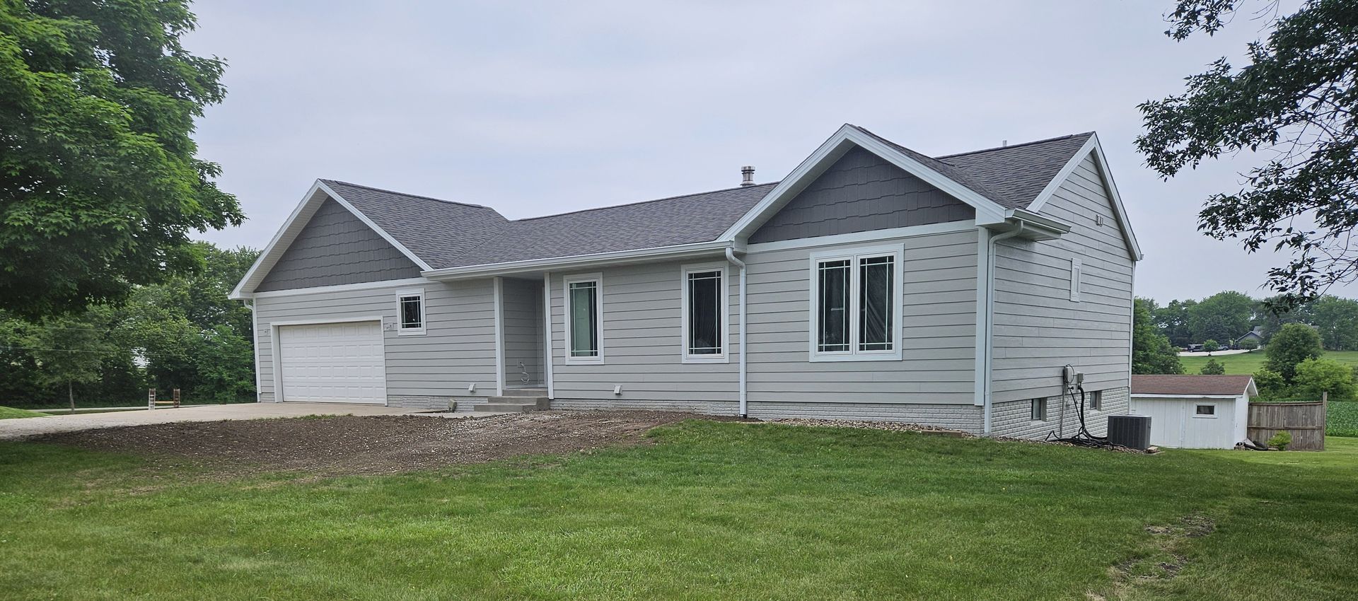 A light gray ranch-style house with a dark gray roof sits on a green lawn.