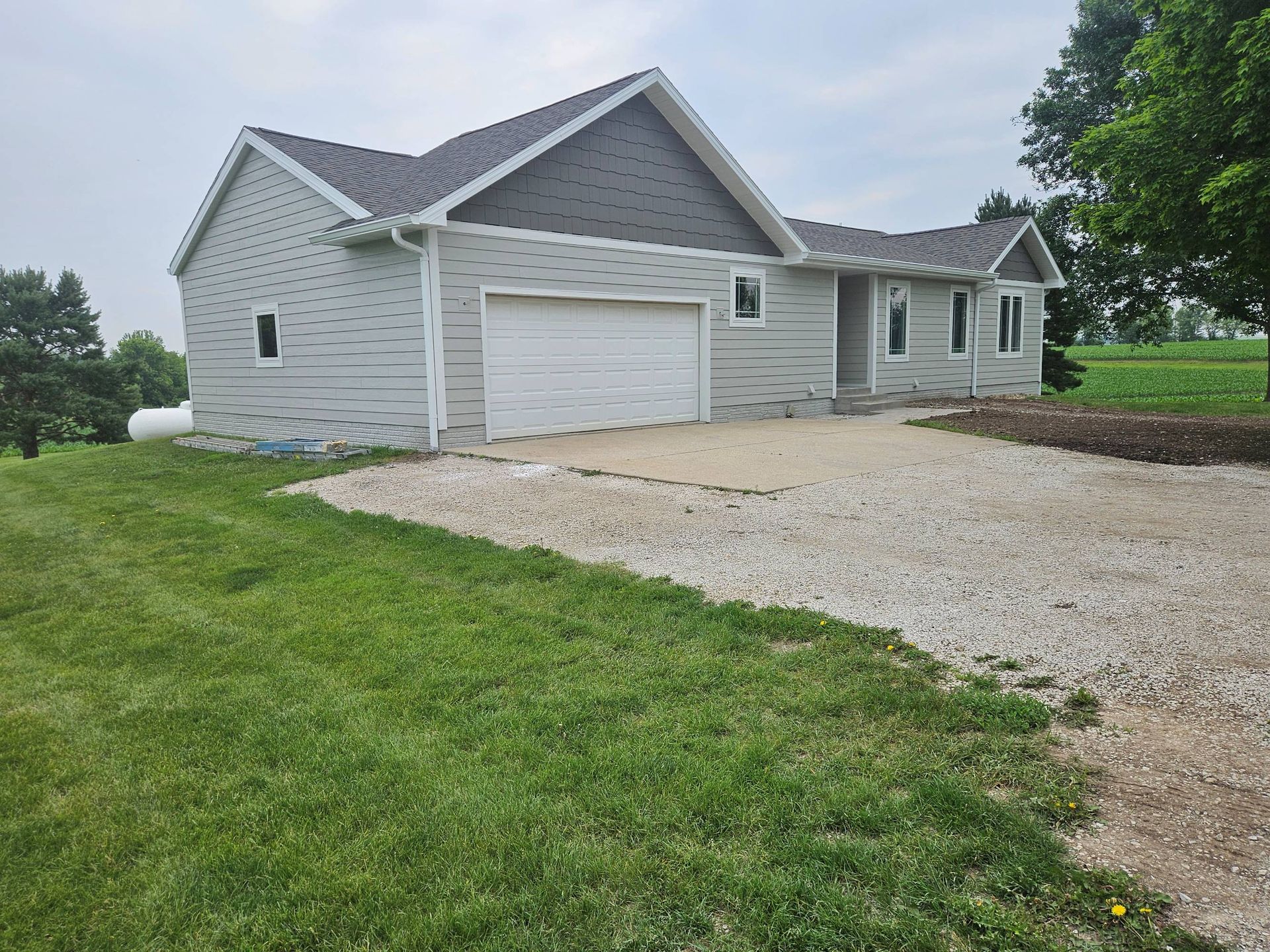 Gray house with attached garage, gravel driveway, and green lawn. Cloudy sky in background.