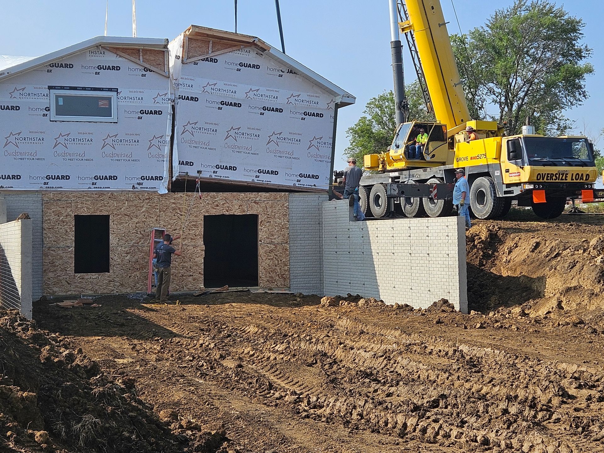 A crane lifting a house section onto a concrete foundation during construction.