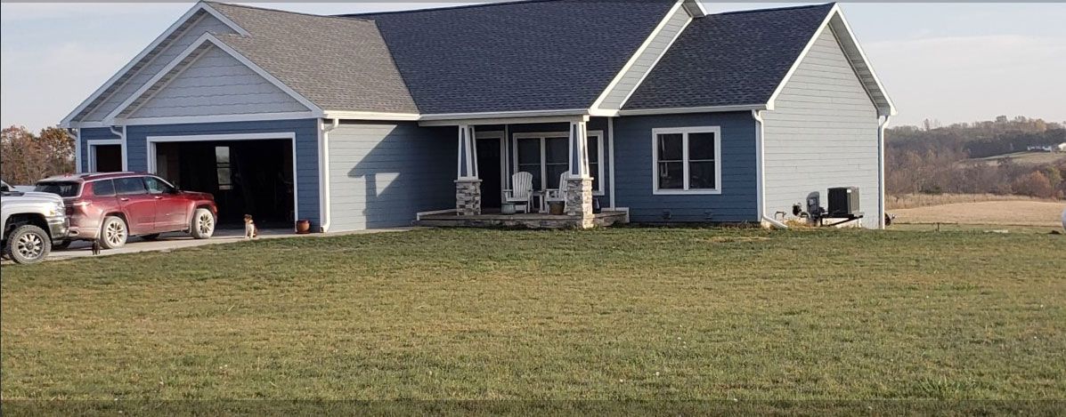 Blue house with attached garage and red vehicle parked inside. Green lawn in front.