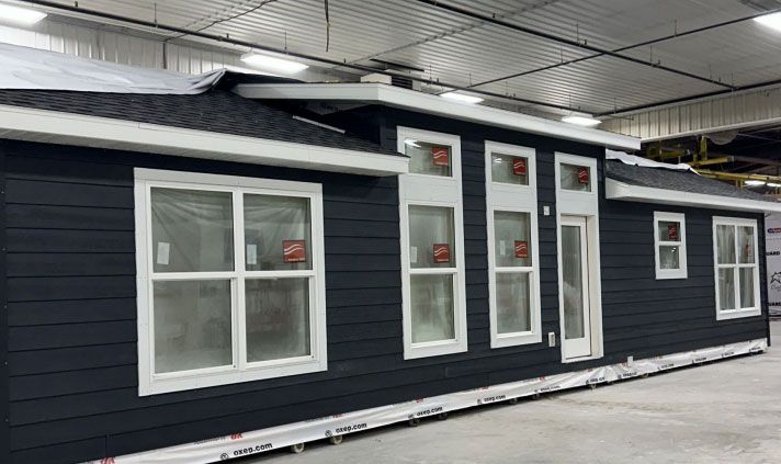 Dark blue manufactured home with white-framed windows, white door, and black roof. Indoor setting.