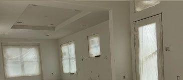 Interior room with white walls, windows covered in plastic, and a ceiling with recessed lighting.