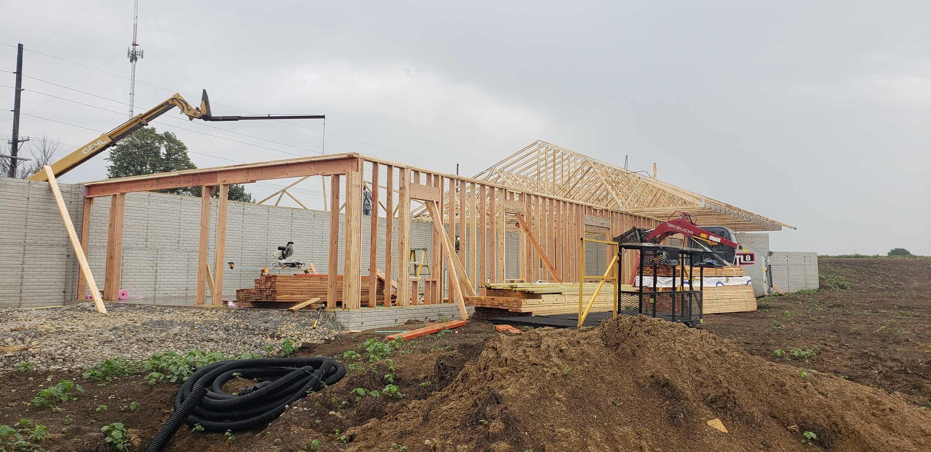 A building under construction with exposed wooden framing and a gray, overcast sky.