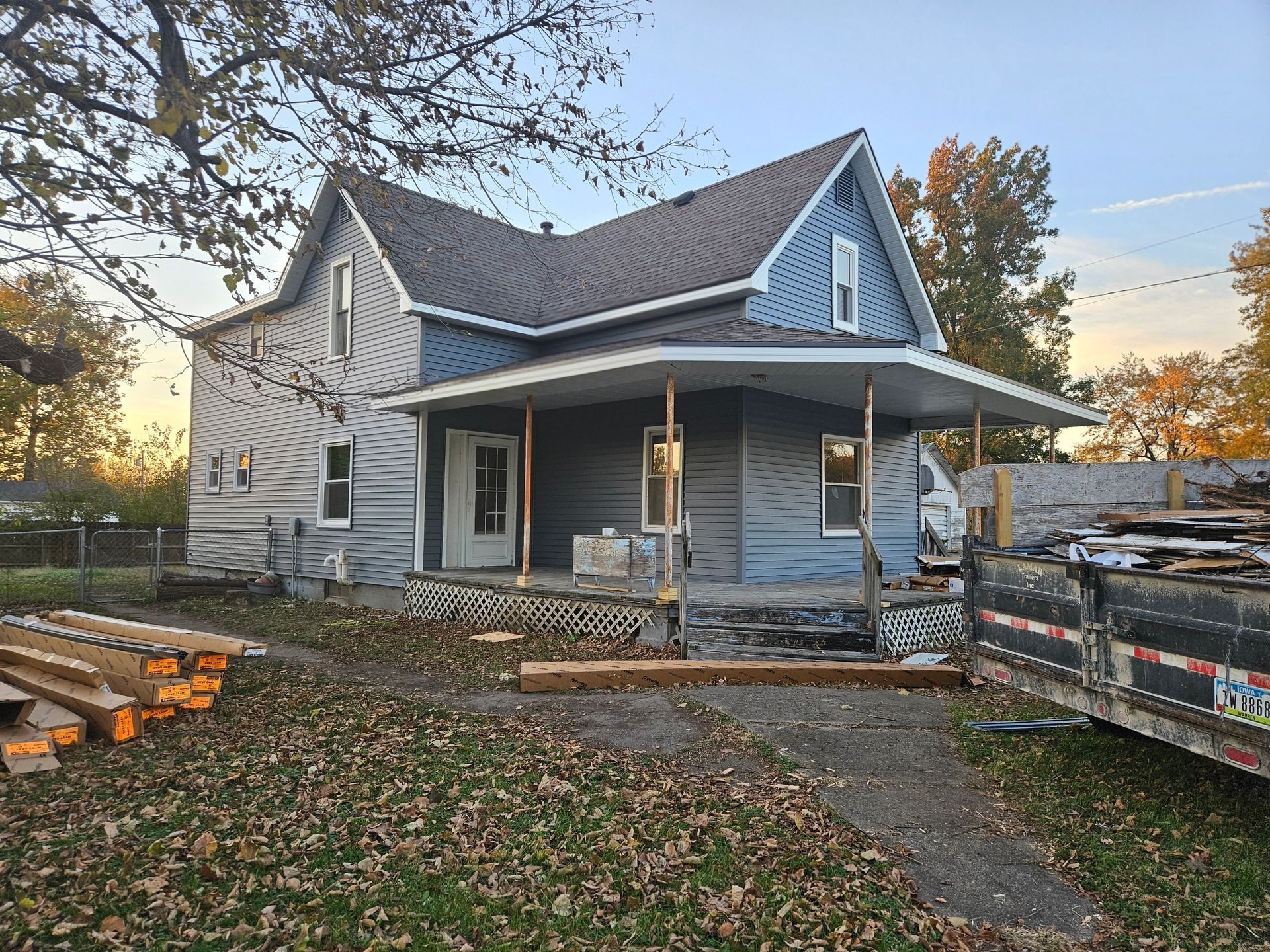 House under renovation with blue siding and a porch. Wood and debris in yard.