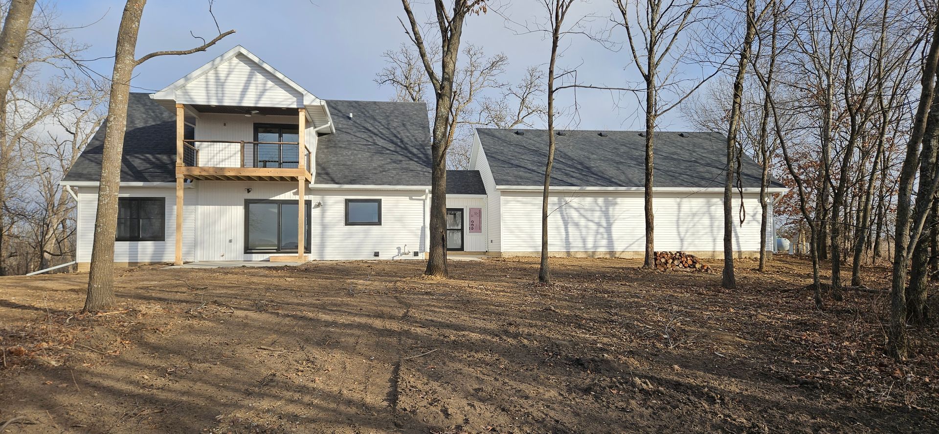 A new white house, with a balcony, under construction amongst leafless trees.