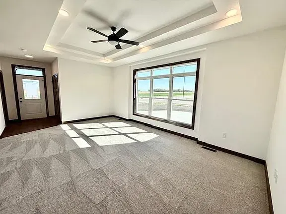 Empty room with gray carpet, a large window, and a ceiling fan.